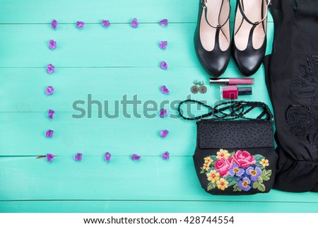 women's clothes - a purple dress, embroidered bag, black heels, earrings, nail polish, lipstick. turquoise wooden background, top view, frame for text