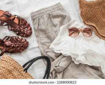 Women's clothing, comfortable vacation clothes - linen trousers, sandals, straw basket, blouse and sunglasses on a light background, top view       - Powered by Shutterstock