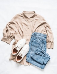 Women's comfortable clothing - oversize blouse, mom's jeans and sneakers on a light background, top view, a Beauty & Fashion Photo by Kiian Oksana