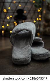 Women's Comfortable Slippers On A Hardwood Cabin Floor With Twinkle Lights In The Background. Moody Dark Setting