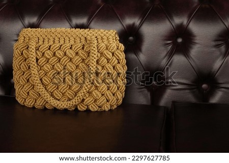 A women's crochet bag on a leather sofa chair.