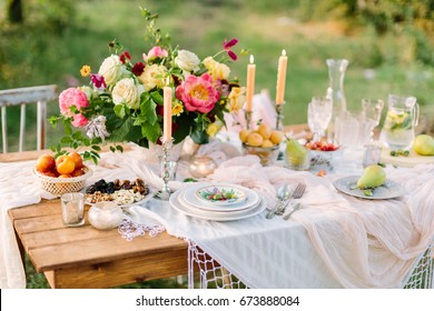 women's day, wedding, celebration, romance, picnic, nature concept - gorgeous table setting with snow white tablecloth, dishes, clear wine-glasses, silver candleholders and various fruits - Powered by Shutterstock