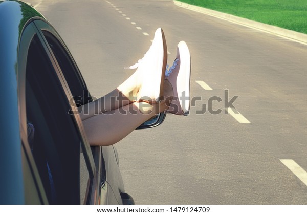 Women\'s feet in the car window on the\
road background. The concept of freedom and\
travel