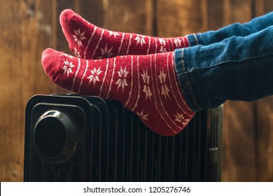 Women's feet in Christmas, warm, winter socks on the heater. Keep warm in the winter, cold evenings. Heating season