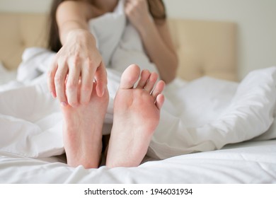 Women's feet. Itching. hand scratches leg. Photo taken in bed with white linens. Made with selective focus and noise effect - Shutterstock ID 1946031934