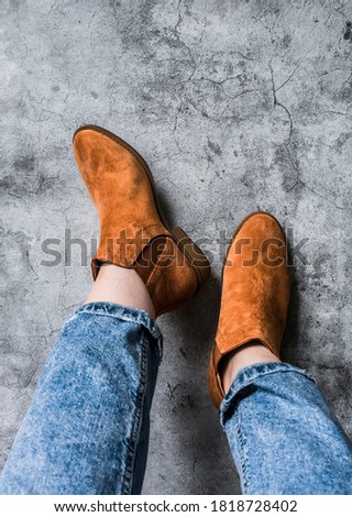 Women's feet in mom's jeans and chelsea suede boots on a gray background, top view