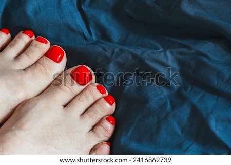 Women's feet with red nails on blue fabric