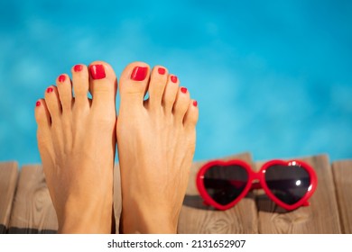 Womens Feet With Red Pedicure Against Blue Water Background. Summer Vacation Concept