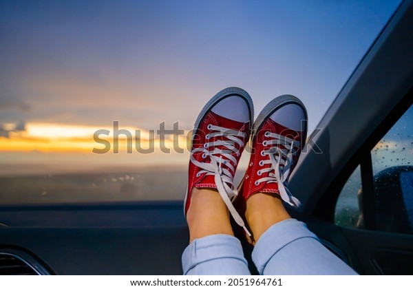 Women\'s feet in red sneakers are lying on the\
dashboard in the car, meeting the\
dawn