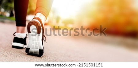 Women's feet in sneakers running on the road web banner. copy space. Young lady running on a rural road during sunset in black sneakers with white sole