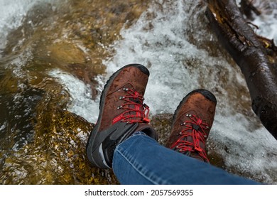 Women's Feet In Trekking Boots On Wet River Stones