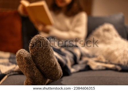 Women's feet in warm woolen socks. Cozy winter evening at home, woman sitting on the sofa with a book