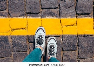 women's feet in white sneakers stand on the pavement one foot stepped on a bright yellow line, cross the line. - Shutterstock ID 1753548224