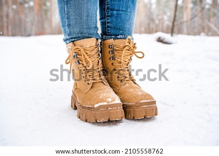 Women's feet in yellow boots in the snow in a snowy forest