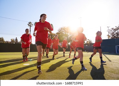 Womens Football Team Run Whilst Training For Soccer Match On Outdoor Astro Turf Pitch