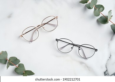 Women's Glasses And Eucalyptus Leaves On Marble Table Top View. 