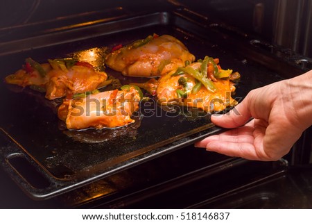 Women's hand holding pan with chicken in curry sauce with peppers and put it in the oven to broil. Daily food.