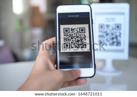 Women's hand uses a mobile phone application to scan QR codes in stores that accept digital payments without money and plastic tags on the table. QR code payment and cash technology concept Foto stock © 