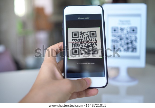 Women\'s hand uses a mobile phone application to\
scan QR codes in stores that accept digital payments without money\
and plastic tags on the table. QR code payment and cash technology\
concept