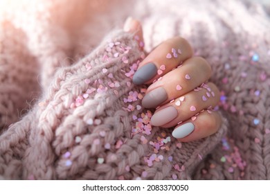 Women's hands with a beautiful matte oval manicure in a warm purple knitted sweater and heart shaped sequins. Winter trend, polish beige nails with gel polish, shellac. Copy space.