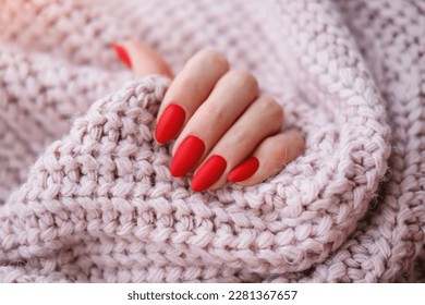 Women's hands with a beautiful matte oval manicure in a warm pink knitted sweater. Winter trend, cover red nails with gel polish, shellac. 