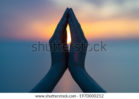 Women's hands in the blue purple sunset as a symbol of yoga or religion, namaste silhouette