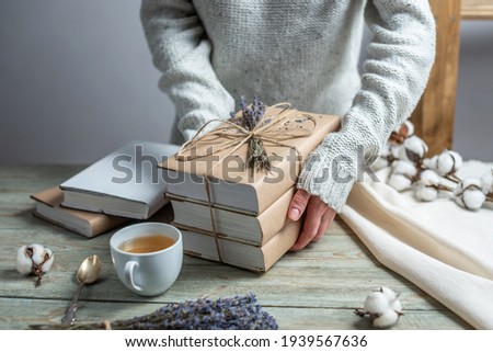 Women's hands are carefully hold a stack of books in craft paper covers, wrapped with rope and decorated with lavender.