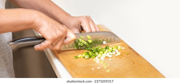 Women's hands cut green onions with a knife on a wooden Board close up with copy space - Powered by Shutterstock