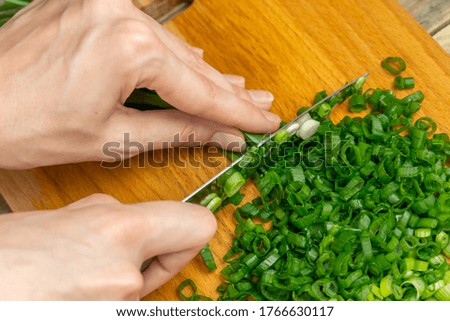 Women's hands cut green onions with a knife on a wooden Board close up