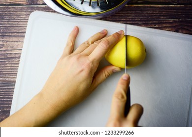 Women's hands cut a lemon in half on a white cutting board. Top view, horizontal, fingers, knife, reamer. Lady hands.