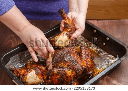 Women's hands cut off a leg from a whole baked chicken in a baking sheet. Horizontal photo.
