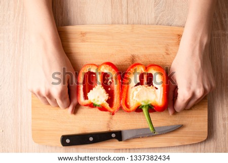 Women's hands cuting a Bell pepper in half on the wooden cutting board