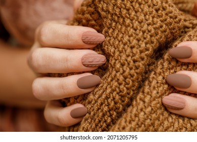 Women's hands with fashionable manicure with a knitted texture on the background of a knitted scarf or plaid. Actual warm shades of autumn in manicure. Matte surface of nail polish. 