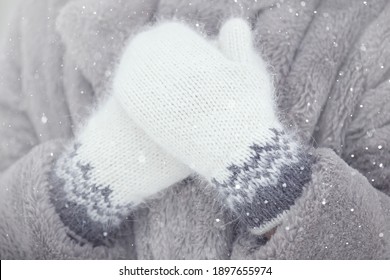 women's hands in hand-knitted down mittens with a pattern on the background of a faux fur coat