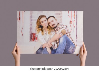 Women's Hands Hang A Family Photo Printed On Canvas Framed In A Stretcher On A Gray Wall