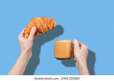 Women's hands hold fresh croissant and cup of coffee  on a blue background. Design concept for breakfast pastry mockup or banner. Free space fot text.