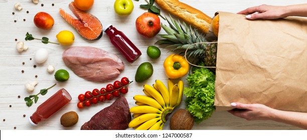 Women's Hands Hold Full Paper Bag Of Groceries Over White Wooden Background, Top View. From Above, Overhead. Flat Lay.