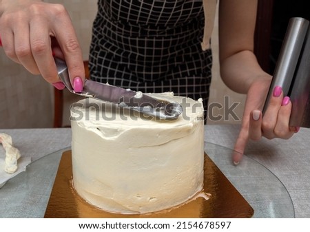 Women's hands hold kitchen spatula leveling the application of cream on top of the cake. Close-up. Selective focus. Picture for articles about food, cooking, confectioners.