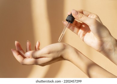 Women's hands hold pipette with cosmetic serum on light brown background, in rays of sunlight. Close-up, copy space. Concept of body care - Powered by Shutterstock