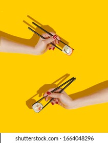 Women's hands hold sushi rolls with sticks. Yellow background. Creative concept