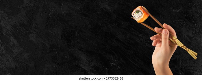 Women's hands hold sushi rolls with sticks. Black background. Creative concept.