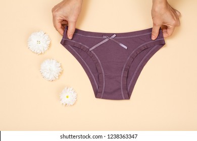 Women's hands holding beautiful cotton brown panties on beige background. Woman underwear set. Top view.