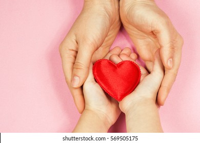 Women's Hands Holding The Child's Hand With A Heart. The Concept Of Motherhood, Caring, Family, Protection, Love. Place For Text. Flat Fly