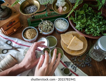 Women's hands holding a tin jar of homemade salve. Home herbalism and cosmetics. Natural homemade salve in metallic tin jar with dried plants and herbs flowers. - Shutterstock ID 2015781941