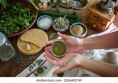 Women's hands holding a tin jar of homemade salve. Home herbalism and cosmetics. Natural homemade salve in metallic tin jar with dried plants and herbs flowers. - Shutterstock ID 2016402749