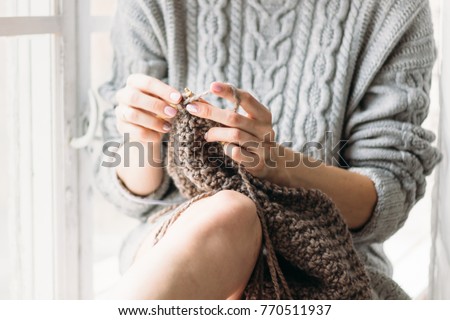 Women's hands knit. The girl knits at the window. Gray sweater.