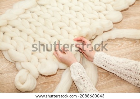 Women's hands knit a plaid of merino wool of large knitting on a wooden floor, top view flat lay. Master class step by step, training