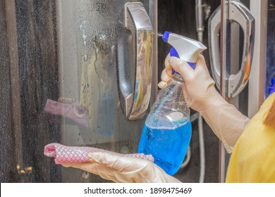 In Women's Hands, A Liquid Blue Detergent In A Bottle And A Rag.Sprays The Product Onto The Dirty Glass Door. Concept-cleaning The Apartment, Room, Bathroom, Shower.The Idea Is Cleanliness And Order.