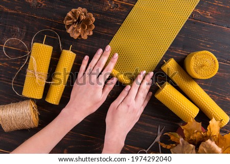 Women's hands make handmade candles from porous wax, on wooden table.