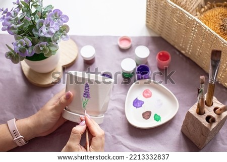 Womens hands paint a white flower ceramic pot on the table. Top view